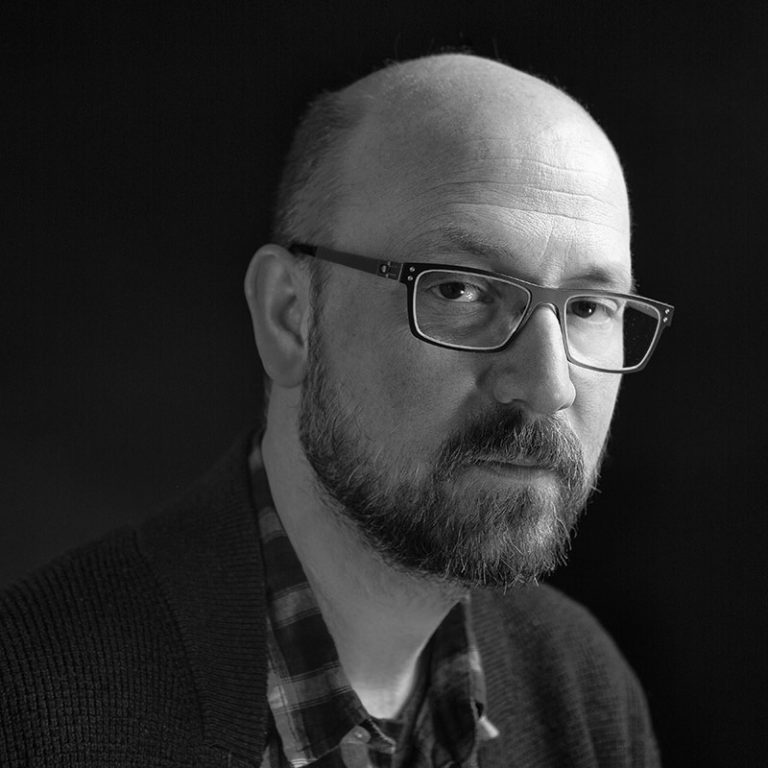 A contemplative man with glasses in a black and white portrait, showcasing a thoughtful expression.