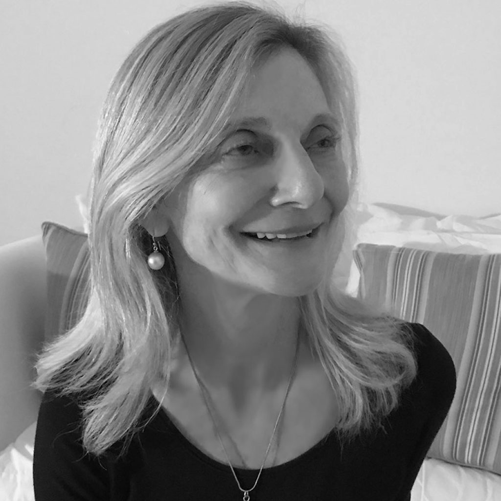 A black and white portrait of a smiling woman with shoulder-length hair, wearing earrings and a necklace, looking off to the side with a gentle expression.