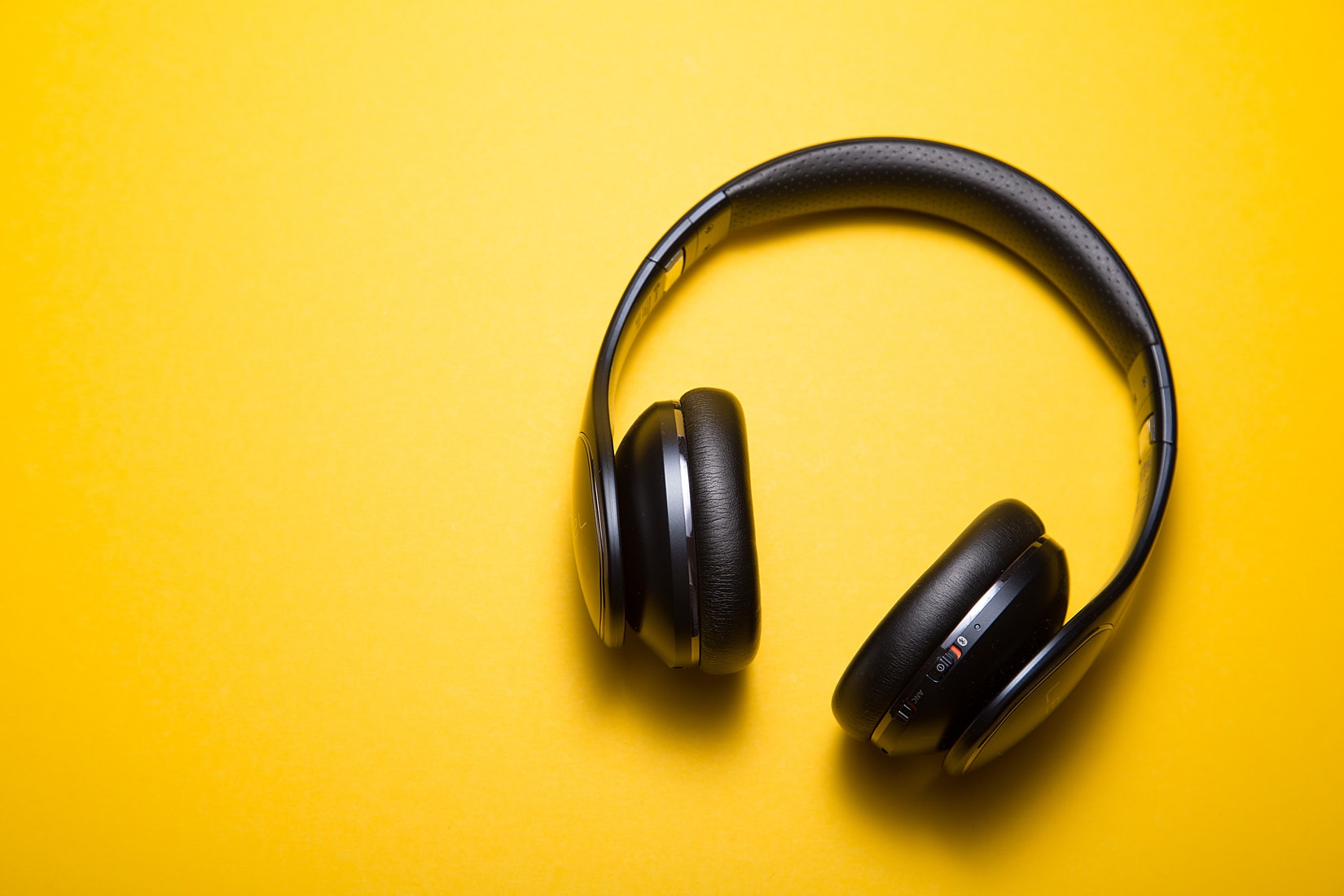 Black wireless headphones against a vibrant yellow background.