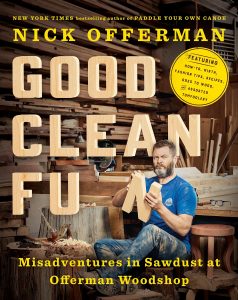 A man with a beard, wearing a blue shirt and denim jeans, sits casually with crossed legs on a woodworking bench surrounded by an array of tools and wooden planks in a rustic workshop environment. he is featured on the cover of a book titled "good clean fun: misadventures in sawdust at offerman woodshop," authored by the man himself, highlighting his adventures and expertise in woodworking.