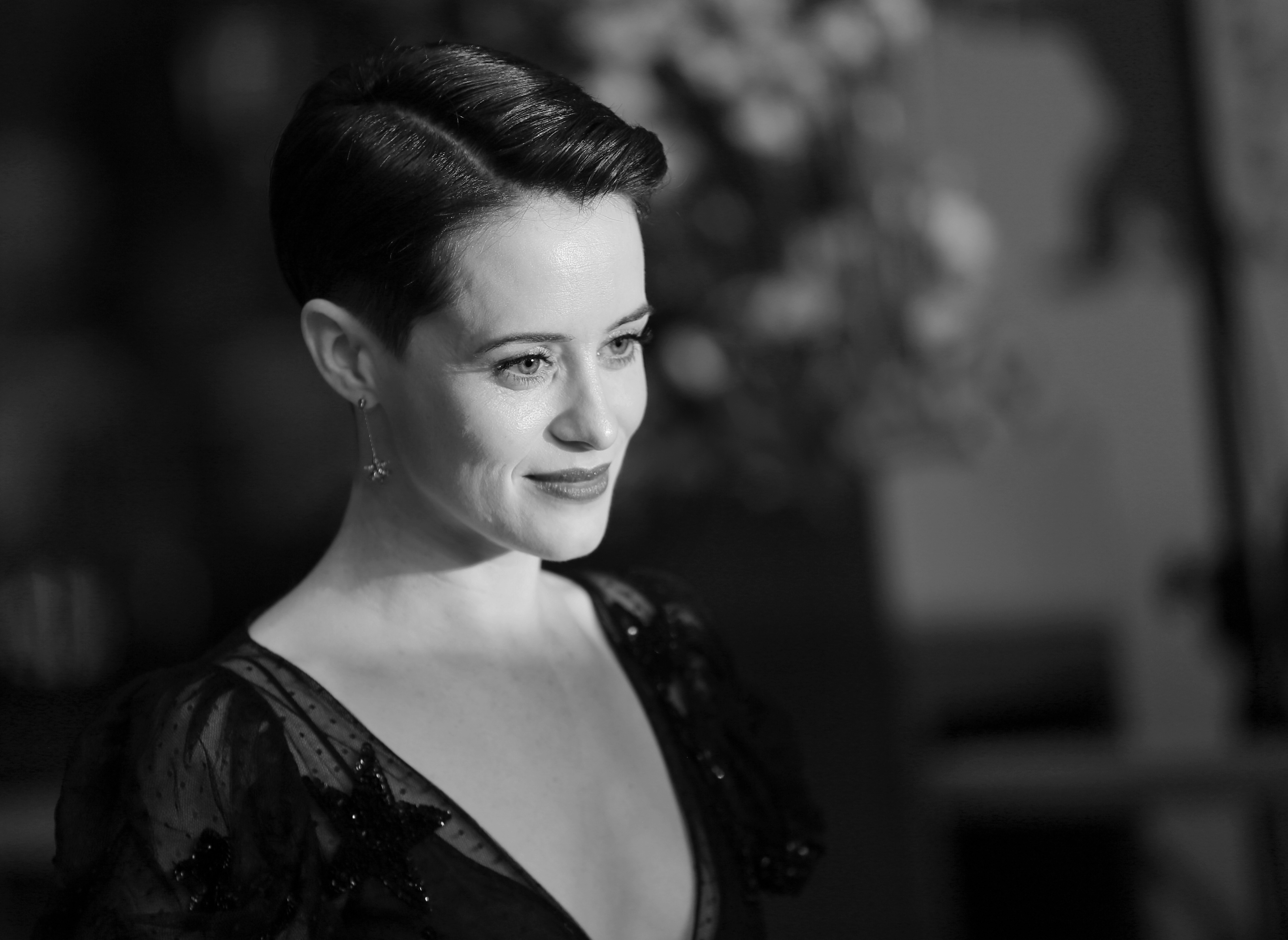 Elegance in monochrome: a woman with a stylish updo hairstyle and a radiant smile, adorned in an embellished dress, glances away from the camera, embodying classic hollywood glamour.