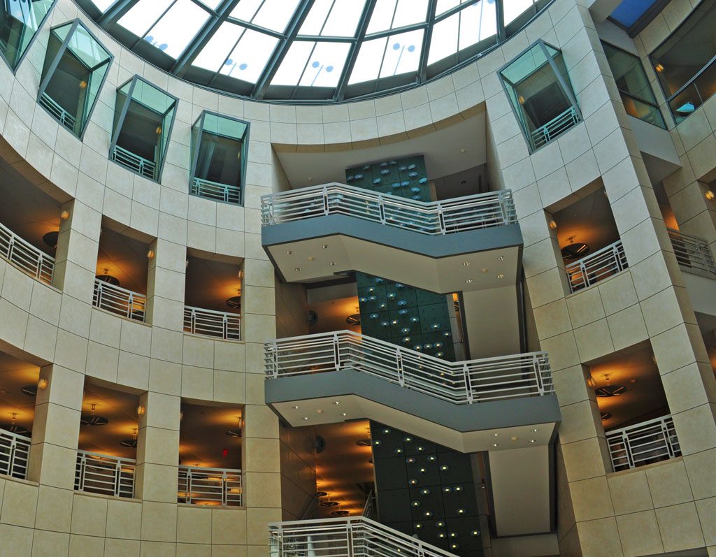 Modern architecture showcasing a spacious atrium with circular design, multiple floors with balconies and a glass ceiling allowing natural light to flood the interior.