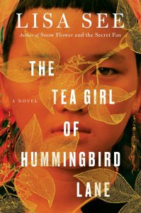 A book cover for "the tea girl of hummingbird lane" by lisa see, featuring a close-up image of a young girl's face with a serious expression, framed by golden leaves against a red background.