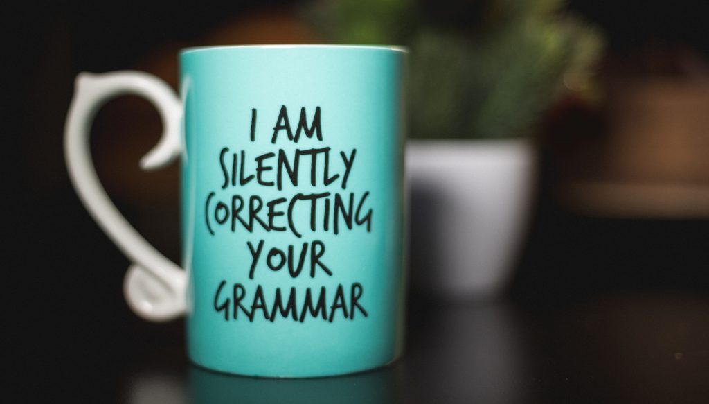A teal mug with the humorous phrase "i am silently correcting your grammar" written on it, suggesting the owner might be a grammar enthusiast or a language professional.