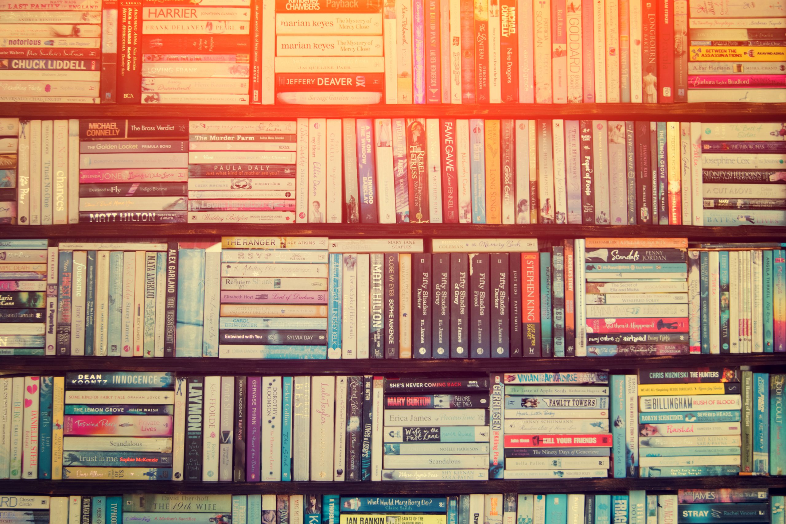 A vintage-toned photograph of multiple wooden shelves filled with a colorful array of well-stocked books, evoking the charm of an old-fashioned library or a book lover's cozy reading nook.