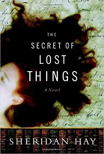 A woman's face emerging from a swirl of dark hair against a background full of cursive writing, representing the cover of "the secret of lost things" by sheridan hay.