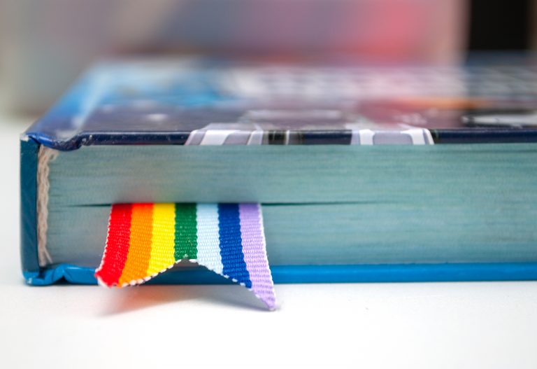A book with pages dyed in a gradient of rainbow colors protruding slightly from the bottom edge, providing a vibrant burst of color.