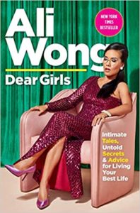 A woman in a sparkling burgundy jumpsuit lounges elegantly on a pink armchair against a green backdrop, with the text "ali wong, dear girls" above and a tagline that reads "intimate tales, untold secrets & advice for living your best life" on a new york times banner.