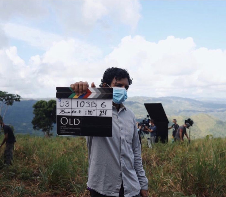 Crew member on a film set holding a clapperboard, with production equipment and picturesque rolling hills in the background.