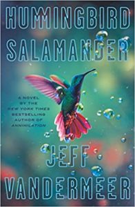 A vibrant novel cover titled "hummingbird salamander" by jeff vandermeer, featuring a hummingbird in mid-flight surrounded by water droplets.