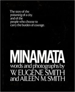 A black book cover with white text that reads: "minamata. the story of the poisoning of a city, and of the people who choose to carry the burden of courage. words by w. eugene smith and aileen m. smith.