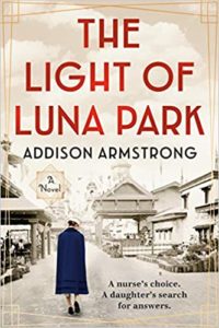 A person in a blue coat walking towards the entrance of an old-fashioned amusement park, as depicted on the cover of "the light of luna park" by addison armstrong—a novel about a nurse's poignant search for answers.