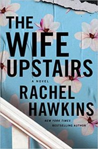 A book cover with a torn paper effect revealing floral patterns underneath, titled "the wife upstairs" by rachel hawkins, noted as a novel by a bestselling author.