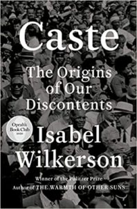 The cover of the book "caste: the origins of our discontents" by isabel wilkerson, featuring a black and white photo of a crowd of people with a mix of expressions, with the book being selected for oprah's book club 2020.