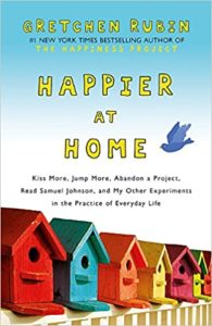 Colorful birdhouses lined up against a sky backdrop, representing the joy of domestic life on the cover of "happier at home" by gretchen rubin.