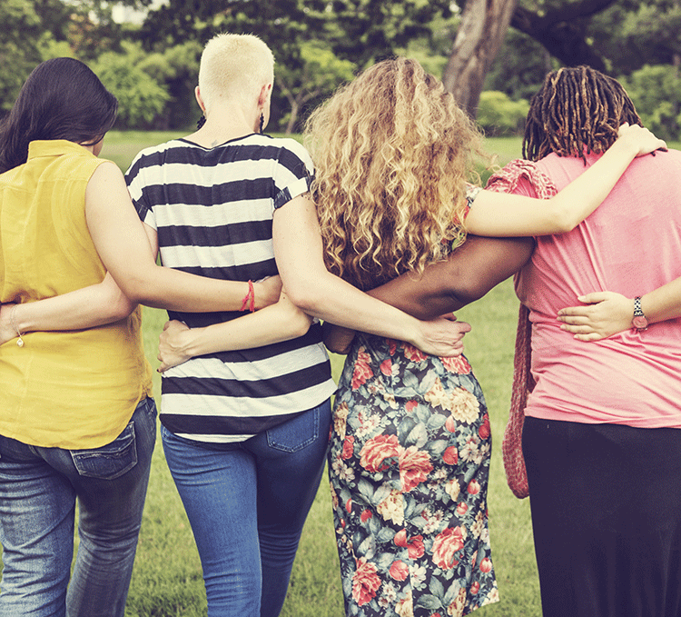 Four friends with their arms around each other, enjoying a moment of closeness in a green park setting.