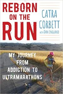 A runner traverses a rural trail amidst a serene landscape on the cover of the book "reborn on the run: my journey from addiction to ultramarathons" by catra corbett with dan england.