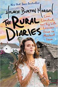 A woman in a relaxed pose with a backdrop of a countryside farm scene on the cover of a book titled "the rural diaries" by hilarie burton morgan. the book promises stories of love, big life lessons, and mischief from the farm.