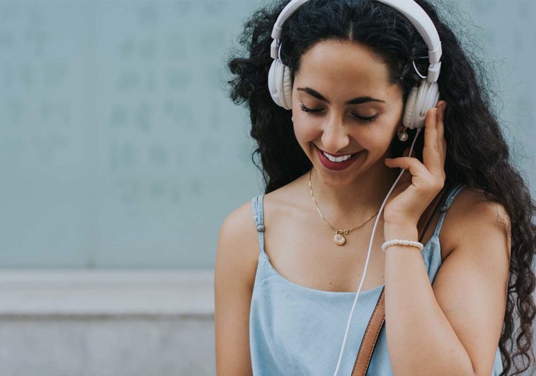 A smiling woman enjoying music with her over-ear headphones outdoors.