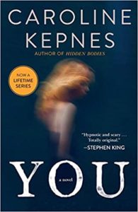 A book cover of the novel "you" by caroline kepnes, featuring a blurred image of a person walking, with a dark backdrop and the recommendation quote "hypnotic and totally original." by stephen king at the top. the cover also includes a badge indicating that it is now a lifetime series.