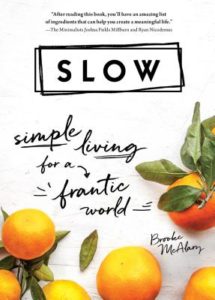 A book cover with a minimalist design, featuring the title "slow" in bold, and the subtitle "simple living for a frantic world." the cover is adorned with fresh oranges and leaves near the top, suggesting a natural and serene lifestyle. the author's name, brooke mcalary, is at the bottom, with a quote praising the book by the minimalists joshua fields millburn and ryan nicodemus at the top.