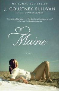 A woman in a red swimsuit lies on a beach, gazing out over the water, on the cover of the novel "maine" by j. courtney sullivan.