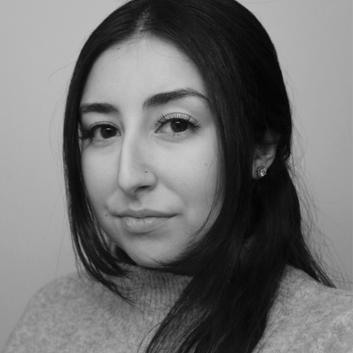 A monochromatic portrait of a woman with a subtle smile, featuring her dark hair and a turtleneck sweater.