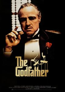 A solemn man in a suit with a rose on the lapel, holding a cigarette, against a dark backdrop with the title "the godfather" prominently displayed below.