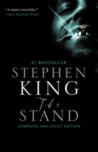 An ominous cover showcasing an eerie grin, with glowing eyes peering through the darkness, sets a chilling tone for stephen king's apocalyptic vision in 'the stand: complete and uncut edition' - a gripping tale of good vs evil.