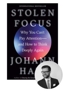 A man in a suit with a thoughtful expression stands adjacent to the cover of the book "stolen focus: why you can't pay attention—and how to think deeply again" by johann hari.