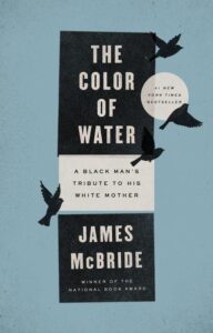 A book cover with a minimalist design featuring the title "the color of water: a black man's tribute to his white mother" by james mcbride, a new york times bestseller and national book award winner. the background is a soft blue with flying birds adding a touch of motion to the composition.