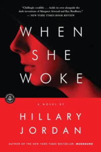 A book cover showcasing a high-contrast image of a woman's profile against a dark background, titled "when she woke" by hillary jordan, with critical acclaim from the new york times book review.