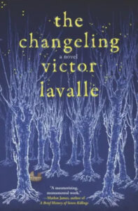 A cover of "the changeling" novel by victor lavalle, featuring an eerie forest formed by white branching trees against a dark blue background, with a small yellow house nestled at the bottom.