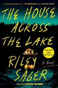 The house across the lake" book cover featuring a dark and atmospheric scene with a solitary house illuminated across a body of water, hinting at a suspenseful and mysterious narrative.
