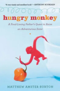 A playful red plastic monkey toy appears to be diving towards a vibrant chili pepper on a bold white background, depicting a scene suggestive of adventurous eating, as promoted by the title of the book "hungry monkey: a food-loving father's quest to raise an adventurous eater" by matthew amster-burton.