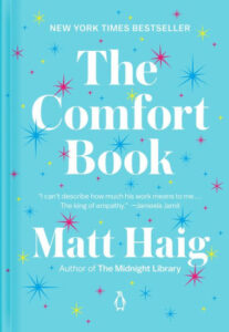 A book cover for "the comfort book" by matt haig, a new york times bestseller, featuring a light blue background with colorful stars and a praise quote by jameela jamil.