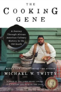 A portrait of michael w. twitty, an african american culinary historian, seated outdoors with traditional cooking implements, gracing the cover of his book "the cooking gene," which delves into african american southern cuisine and its history, with accolades for winning the james beard award.