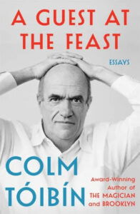 The image is a book cover for "a guest at the feast" featuring essays by colm tóibín, an award-winning author known for "the magician" and "brooklyn." the cover showcases the author's portrait with an intense and thoughtful expression, set against a light background. the title and author's name are prominently displayed in bold, contrasting colors.