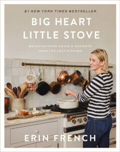 A woman cooking in a cozy kitchen with a warm smile, surrounded by a rustic ambiance and cooking utensils, representing the heartwarming theme of the cookbook "big heart little stove" by erin french.