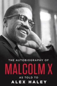 A thoughtful man in glasses, smiling and resting his cheek on his hand, on the cover of "the autobiography of malcolm x" as told to alex haley.
