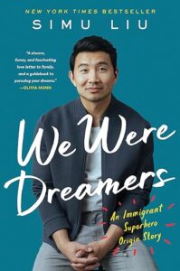 A man in a smart-casual outfit leans against a teal background above the title "we were dreamers: an immigrant origin story," touted as a new york times bestseller with a quote of endorsement from olivia munn.