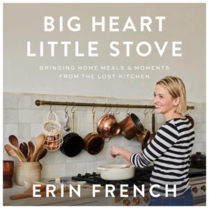 A woman happily cooking in a homey kitchen with the caption "big heart little stove - bringing home meals & moments from the lost kitchen - erin french".