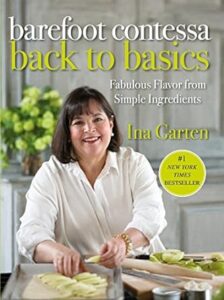 Woman in a kitchen smiling while cooking, featured on the cover of "barefoot contessa back to basics" cookbook.