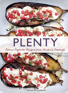 Grilled eggplants topped with fresh pomegranate seeds, presented on a rustic surface, embodying a dish from yotam ottolenghi's "plenty" cookbook featuring vibrant vegetable recipes.