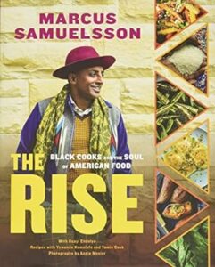 A cheerful man wearing a yellow hat and a vibrant, patterned scarf smiles against a golden background, next to images of delicious food, on the cover of a book titled "the rise: black cooks and the soul of american food" by marcus samuelsson.