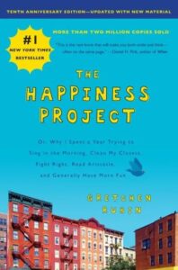 A vivid cover of the book "the happiness project" by gretchen rubin, showcasing a lively street scene with the book's title and accolades prominently displayed.