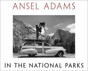 A vintage car parked in a scenic national park with a photographer standing on top, using a large format camera to capture the majestic landscape.