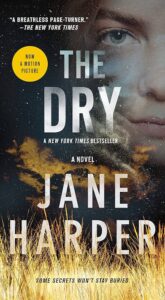 Book cover of "the dry" by jane harper, featuring a close-up of a woman's face partially obscured by tall, dry grass and text proclaiming it a motion picture and a new york times bestseller.