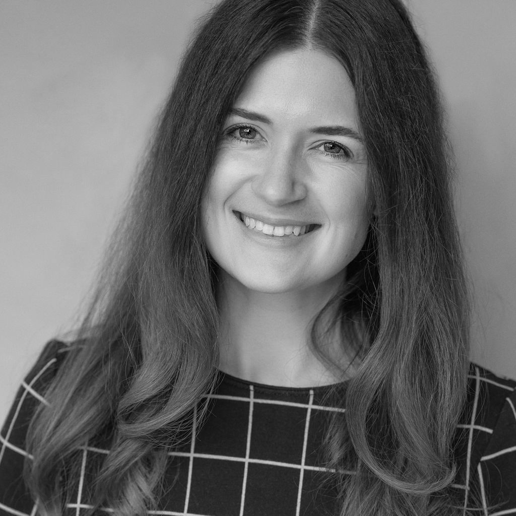 Black and white photo of a smiling woman with long hair, wearing a checkered top.