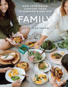 A group of people enjoying a meal with various vegetarian dishes, with the book cover text "Family" by Hetty McKinnon.